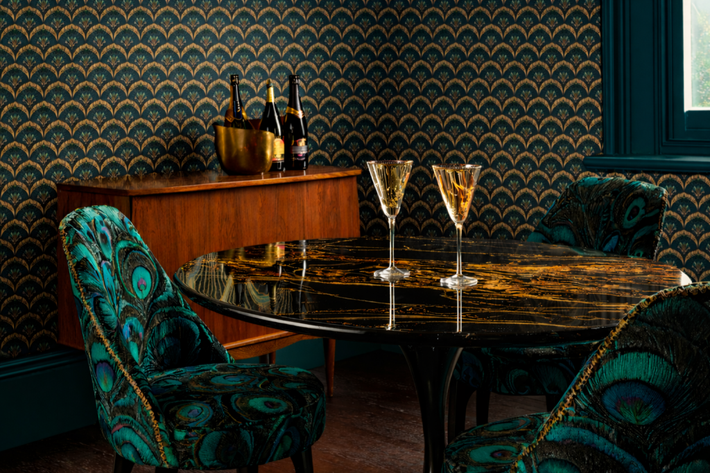 A dramatic Art Deco style dining corner with fan-design black, gold and teal wallpaper, peacock tail upholstered chairs and a black marble table