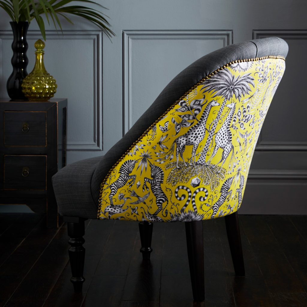 Upholstered accent chair with grey velvet fabric and a bright yellow jungle pattern fabric on the back