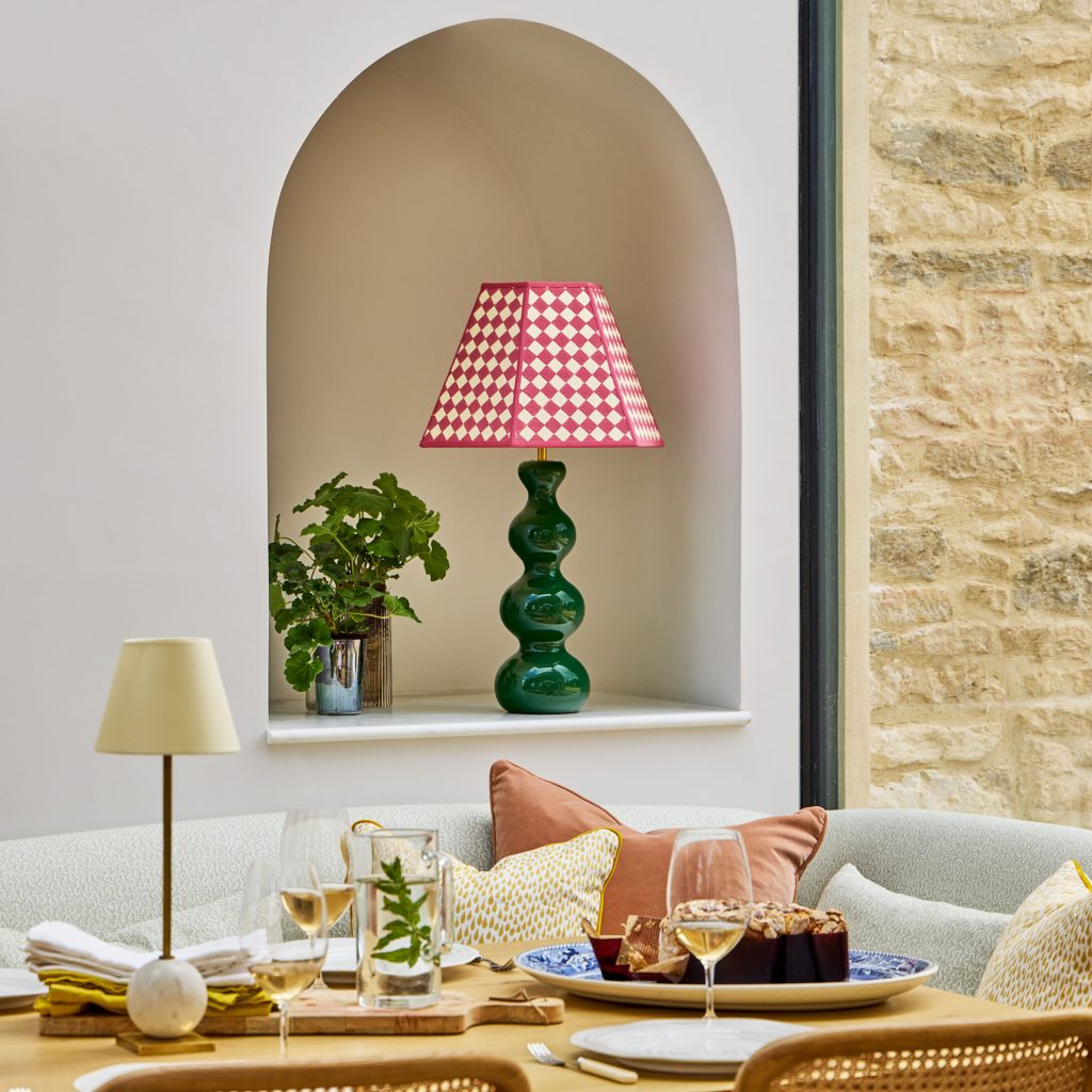 Dining area with neutral colour scheme, a bold green table lamp with red and white checquered shade on a shelf