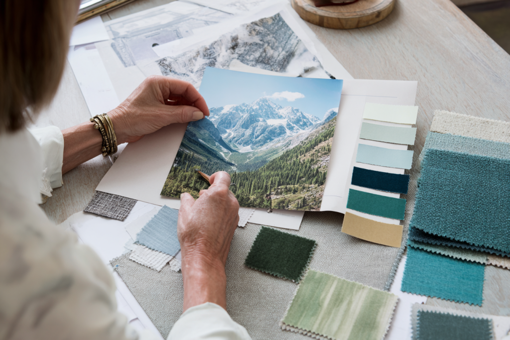 A close up of a mood board in preparation, with an image of a mountain landscape and various paint and fabric samples surrounding it.